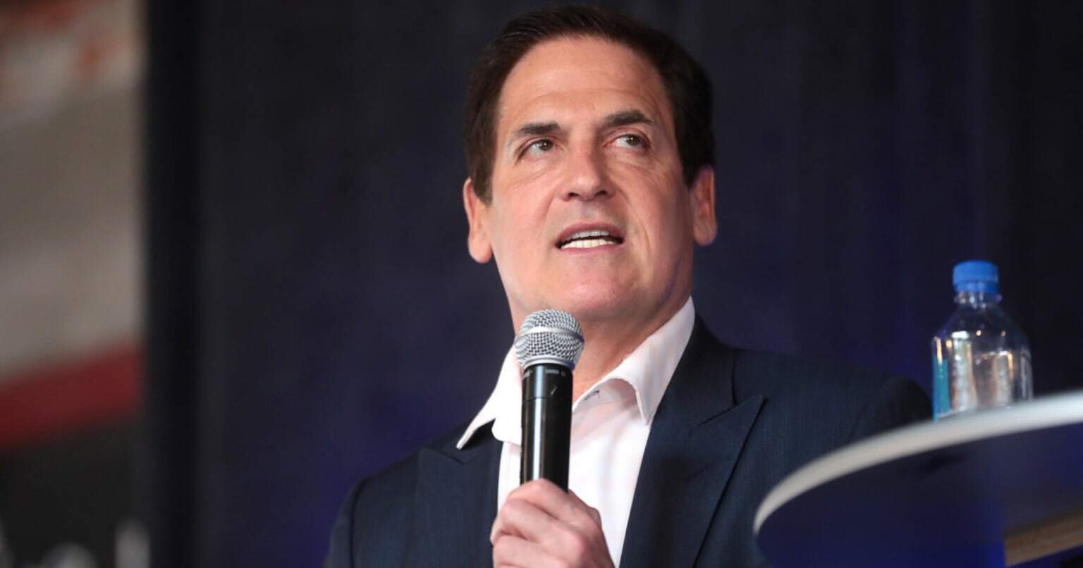 A businessman speaks into a handheld microphone during a public event.