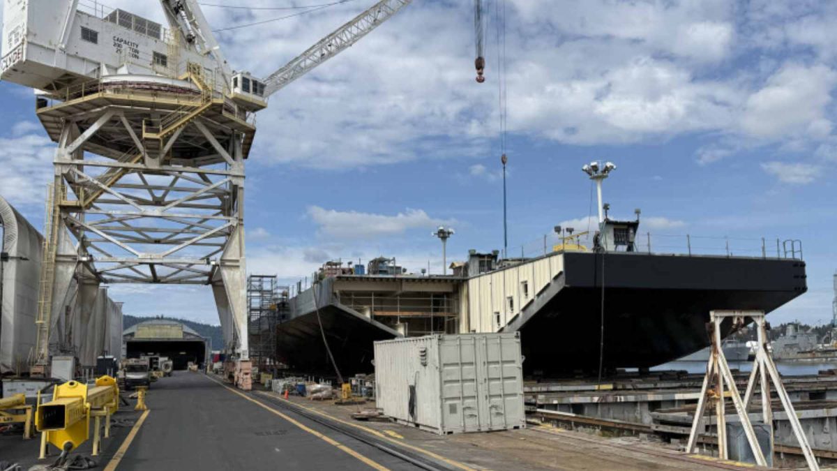 A wide view of a modern industrial shipyard with naval vessels under construction and heavy cranes.