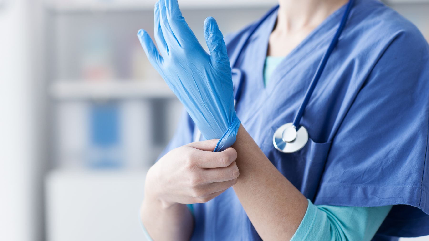 A health care worker in scrubs puts on blue medical gloves, reflecting Texas efforts to expand the physician workforce through HB 2038.