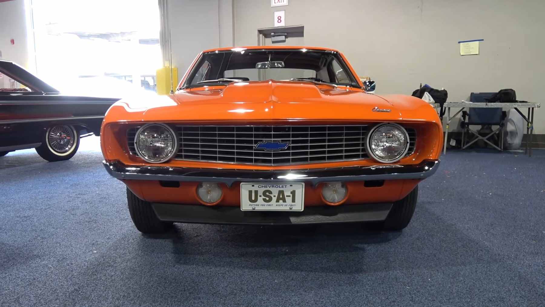 A restored Hugger Orange 1969 Chevrolet COPO Camaro with a 427 cubic inch engine on display at a concours muscle car show.