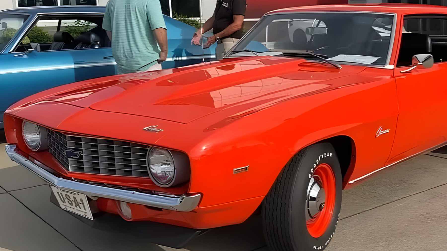 : A restored Hugger Orange 1969 Chevrolet COPO Camaro with a 427 cubic inch engine on display at a concours muscle car show.
