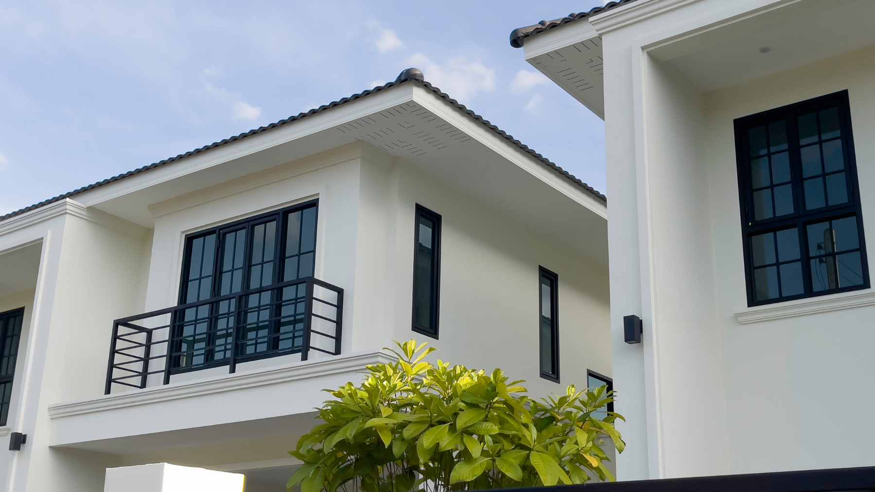 A modern white two-story house featuring large black-framed windows made of high-security laminated glass.