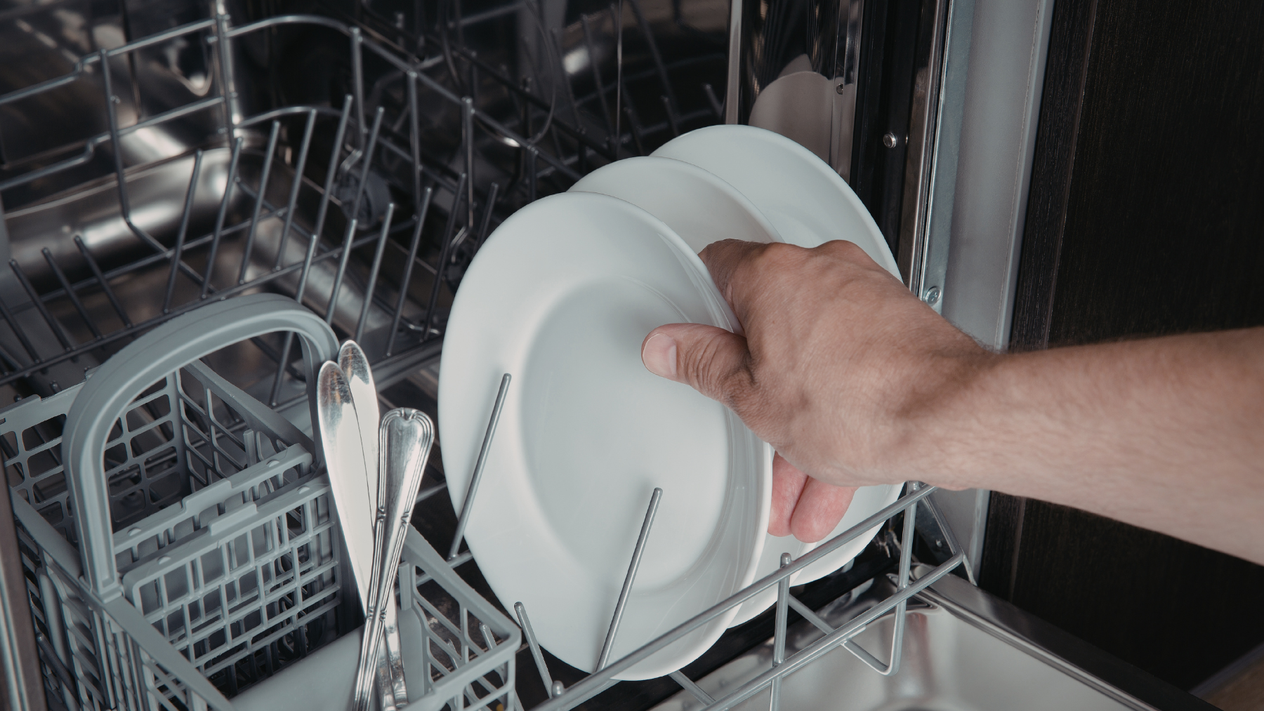 A person cracking open a dishwasher door a few inches to let steam escape immediately after a cleaning cycle.
