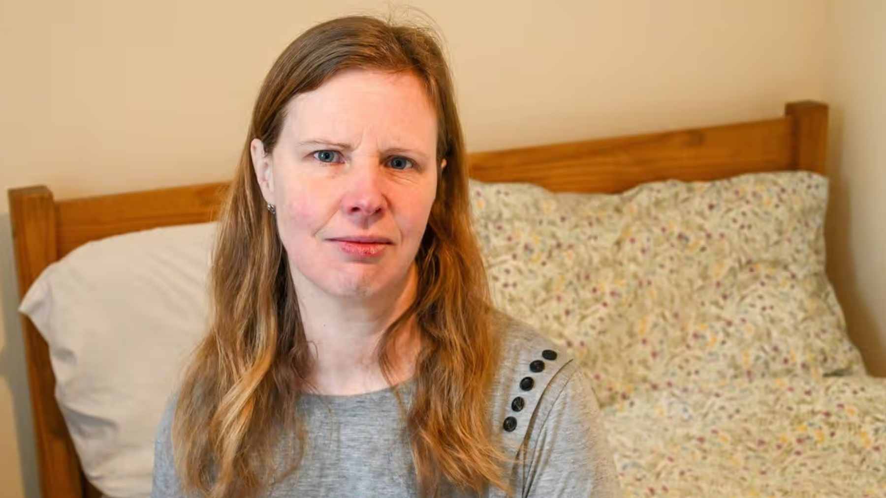 Jennifer Barton, a victim of a celebrity romance scam, looking distressed while holding her phone in temporary housing.