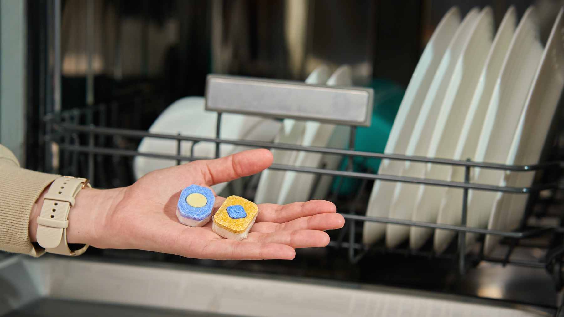 A close-up shot of a dirty oven door being cleaned with a dampened dishwasher tablet, revealing a sparkling surface underneath.
