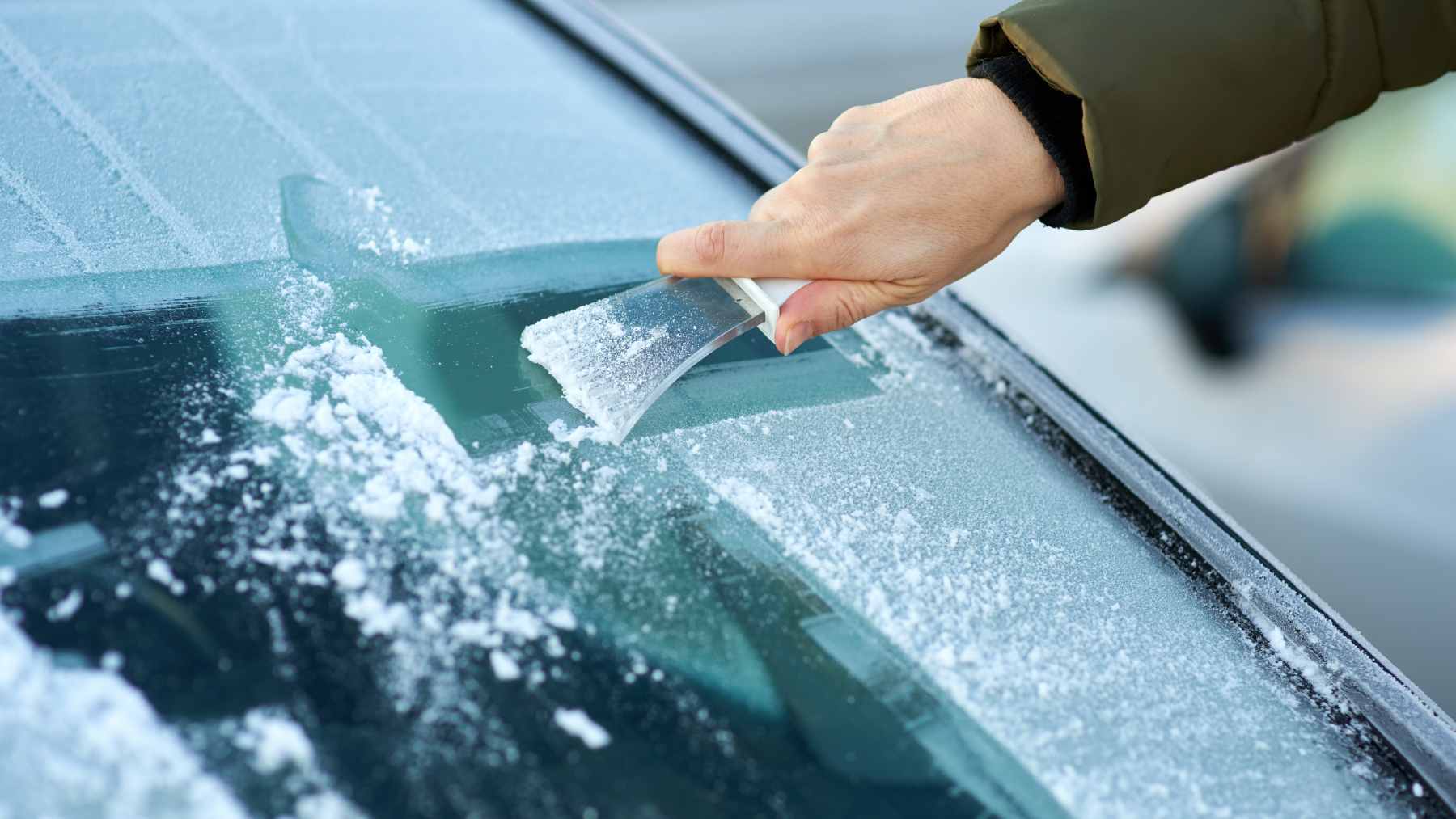 A person spraying a homemade vinegar and water solution onto a car windshield to prevent frost and ice buildup.