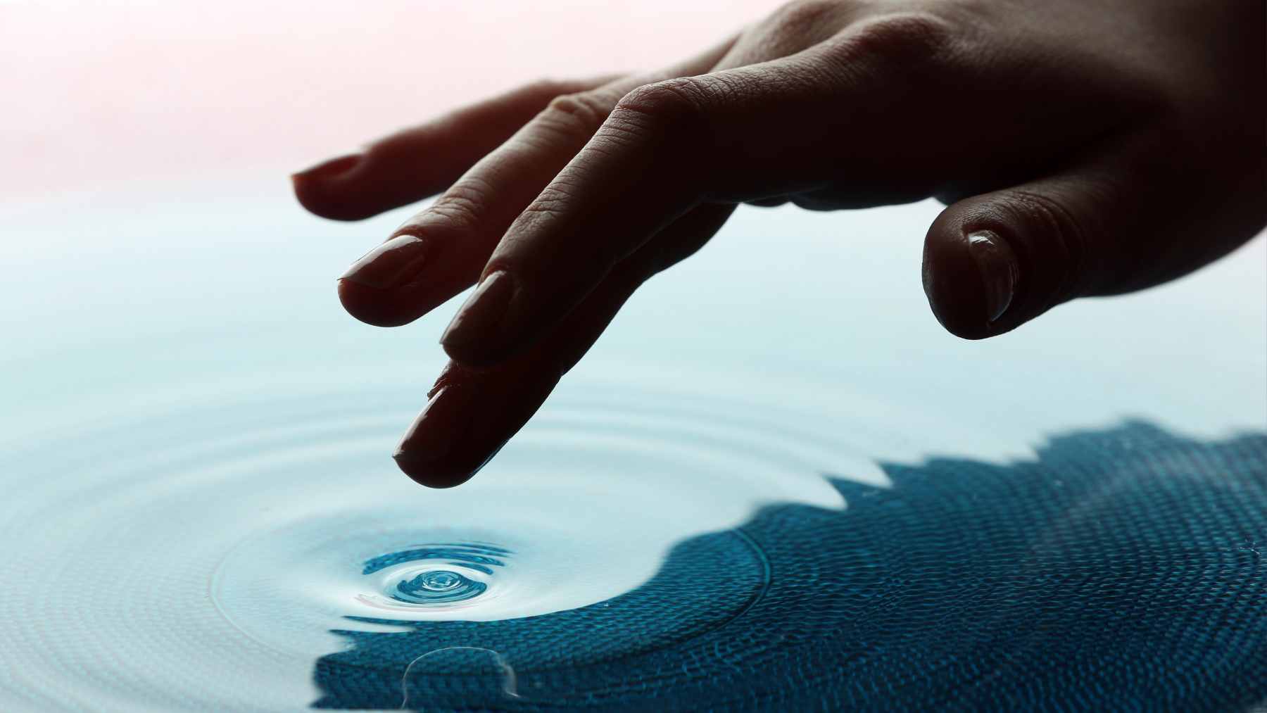 A close-up of a human finger moving through a container of sand during a scientific experiment on remote touch.