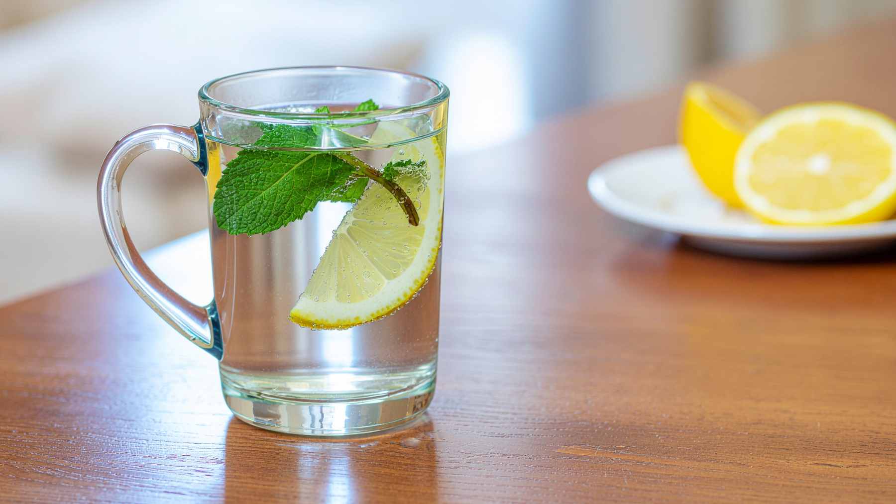 A glass of water with fresh lemon slices and a squeeze of juice, illustrating a daily hydration habit.