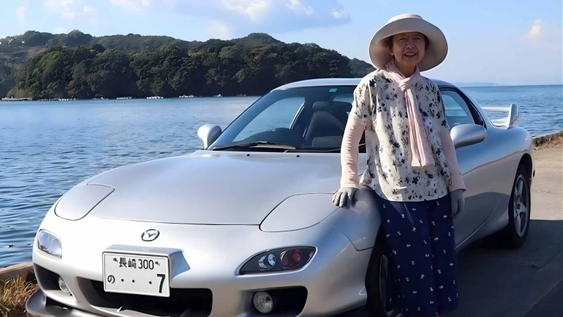Naoko Nishimoto, 80, shaking hands with a Mazda representative next to her silver 1999 Mazda RX-7.