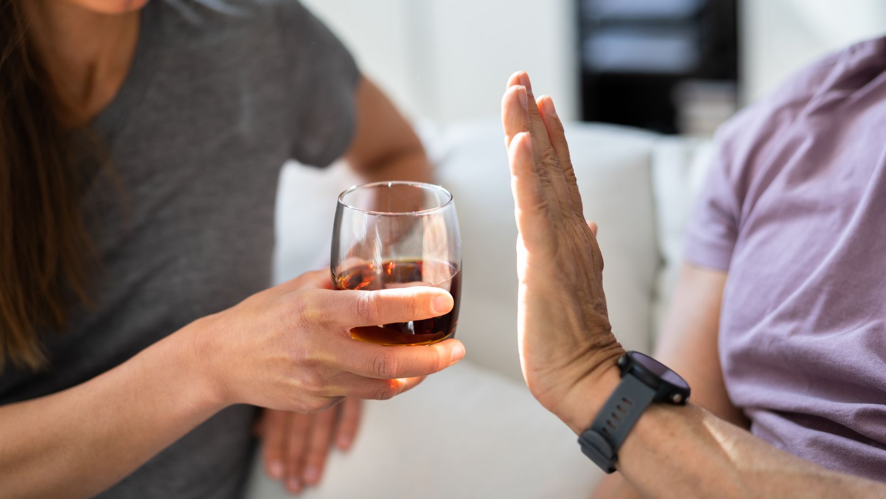 An older adult looking at a glass of red wine while a neurologist's warning about alcohol and brain health appears in the background.
