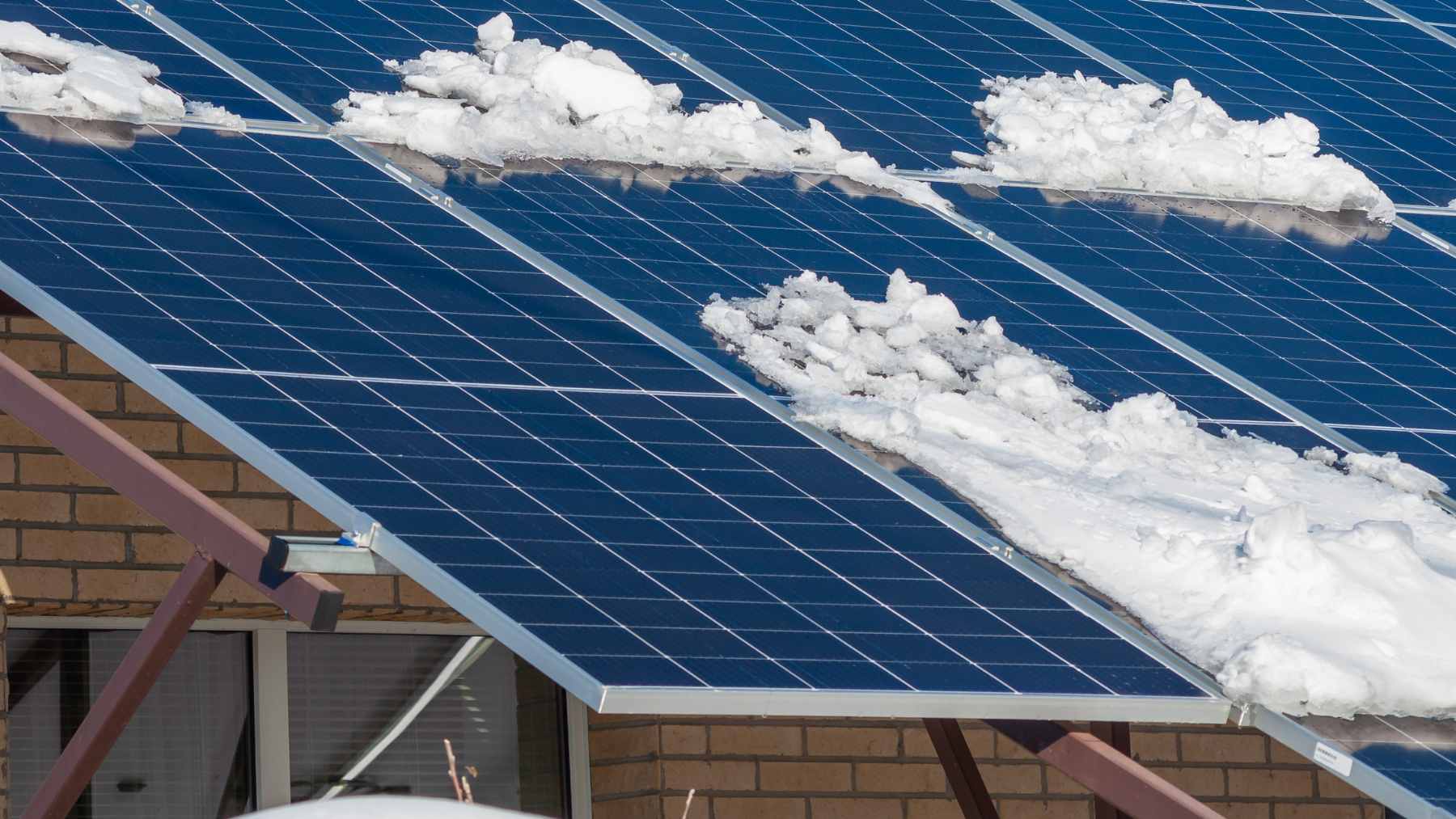 A tilted rooftop solar panel array with a light dusting of snow, illustrating winter energy production and the albedo effect.
