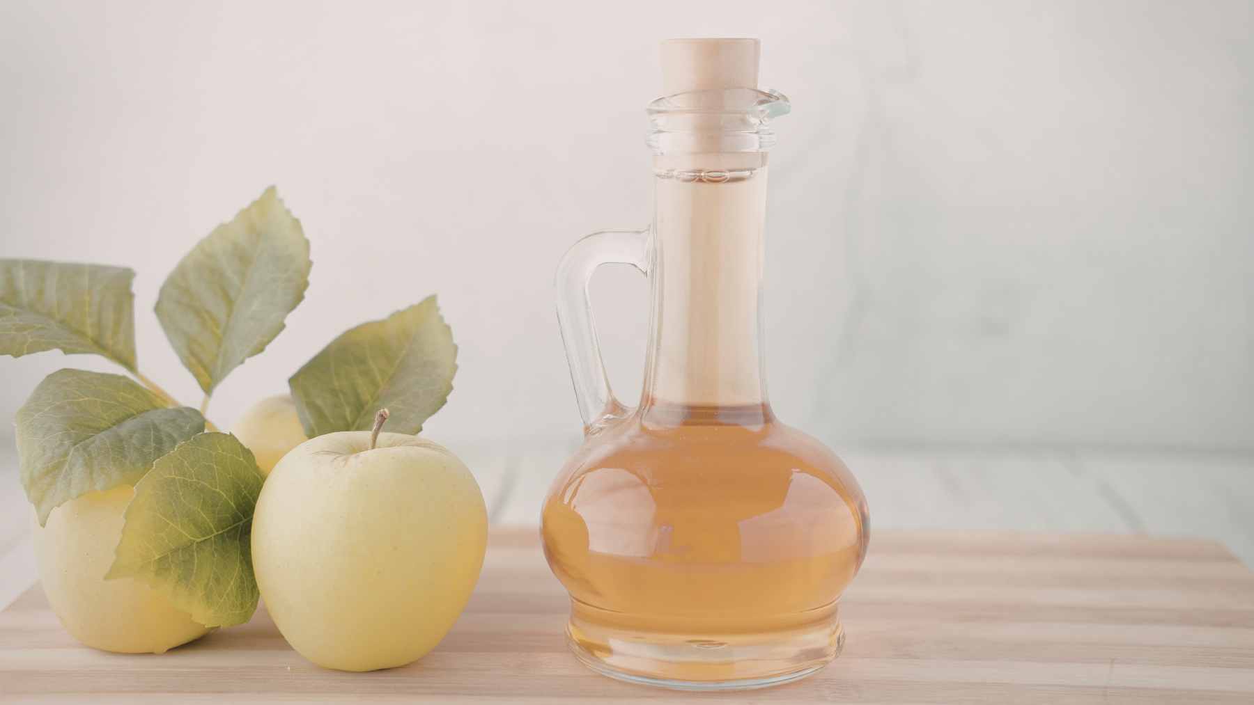 A person using a spray bottle with a vinegar solution to clean the floor and baseboards under a wooden bed frame.